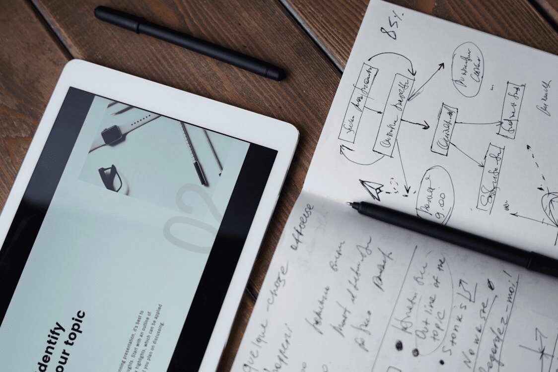 10 Proven Tips for Finding Help with Your Marketing Strategy 7 A tablet displaying a graphic alongside a notebook filled with handwritten notes and sketches on a wooden surface. 10 Proven Tips for Finding Help with Your Marketing Strategy