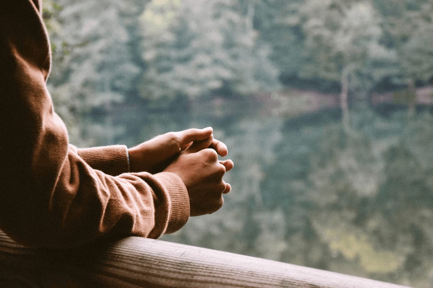 Close-up of a person with crossed arms resting on a wooden railing, looking out over a tranquil water surface surrounded by trees. Calming Techniques for When Your Thoughts Feel Out of Control