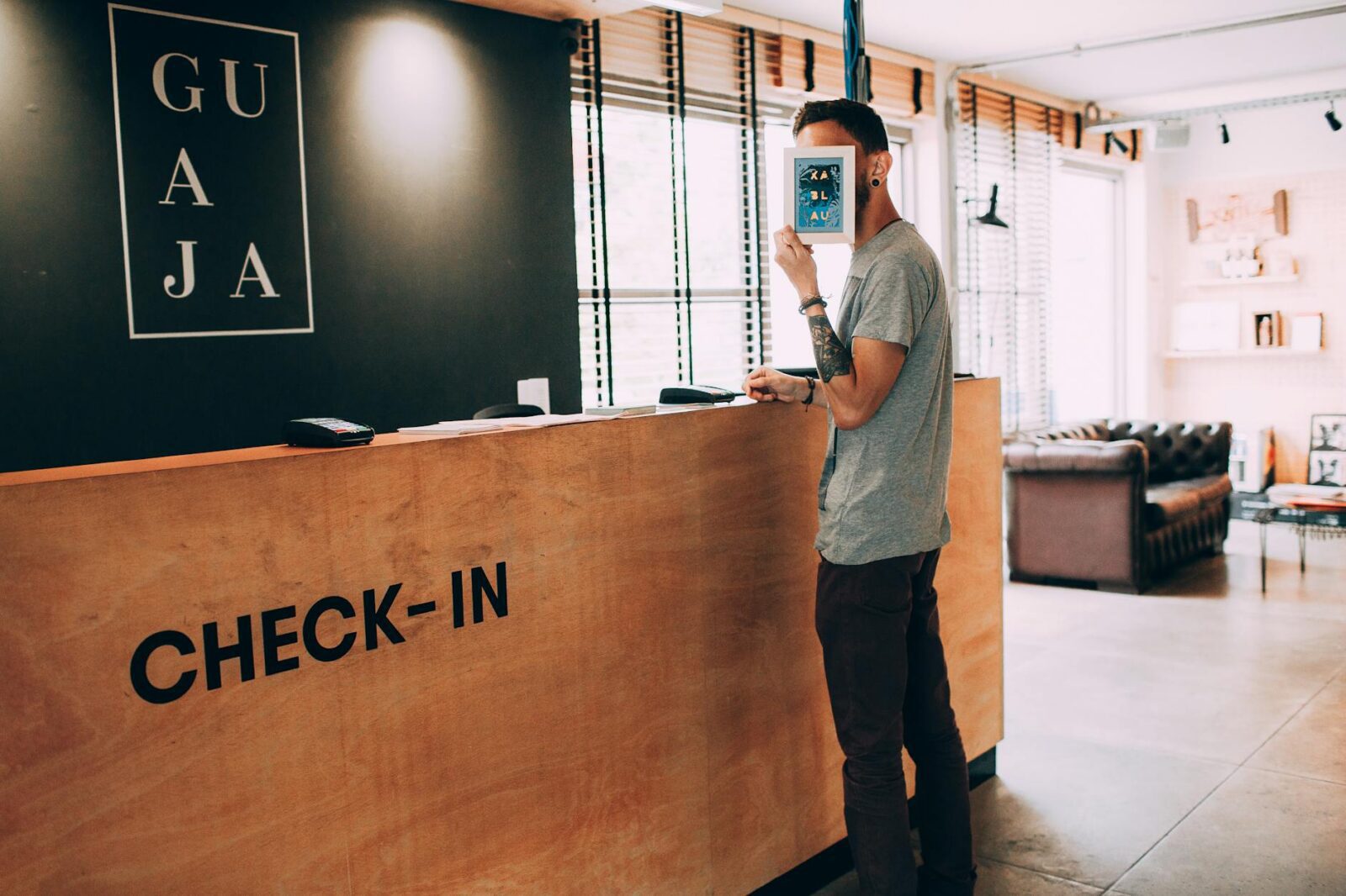How to Increase Hotel Revenue: 3 Practical Tips for Sustainable Growth 9 man covering face with frame at the check in counter of a hotel lobby How to Increase Hotel Revenue: 3 Practical Tips for Sustainable Growth